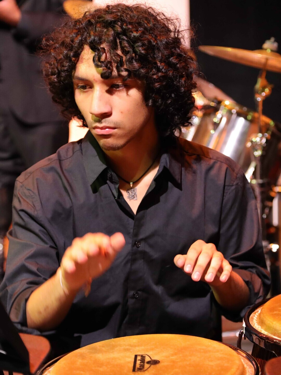 A music student looks intensely at a music stand over a drum with hands poised to strike. 
