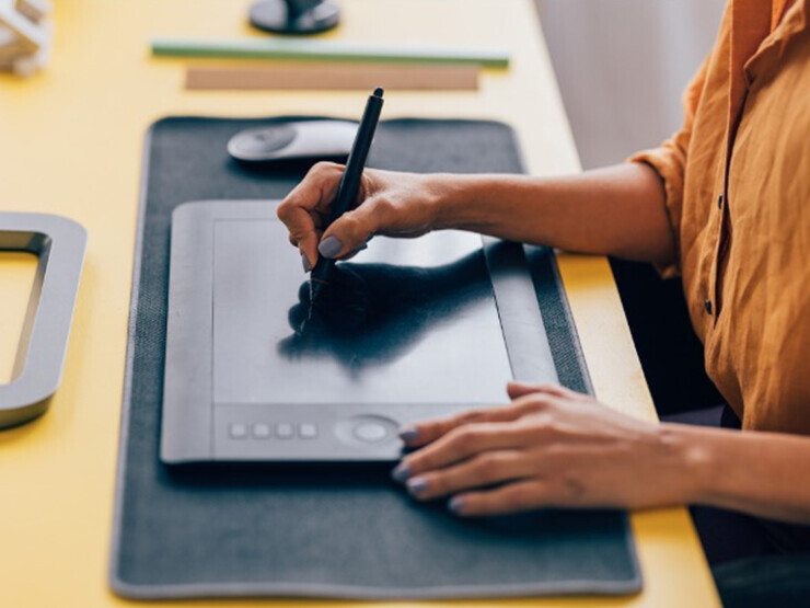 A hand uses a drawing pen to write on a drawing tablet. 
