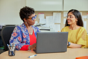 Two people converse in front of a laptop.