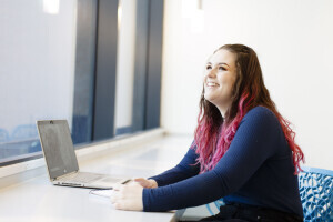 Student smiling while sitting behind a laptop.