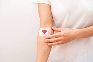 An arm wears a white bandage with a red heart on it. 