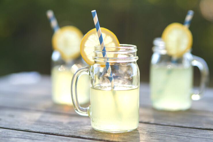 links to Mugs of lemonade topped with lemon slices and striped straws. 