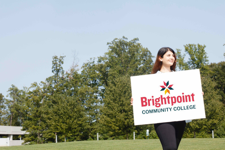 Woman standing in field holding sign featuring college logo