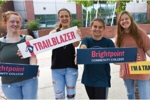 A group of Brightpoint students smile and hold signs with the Brightpoint logo and mascot name. 