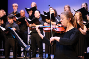 A violinist plays with the Brightpoint Chorus in the background. 