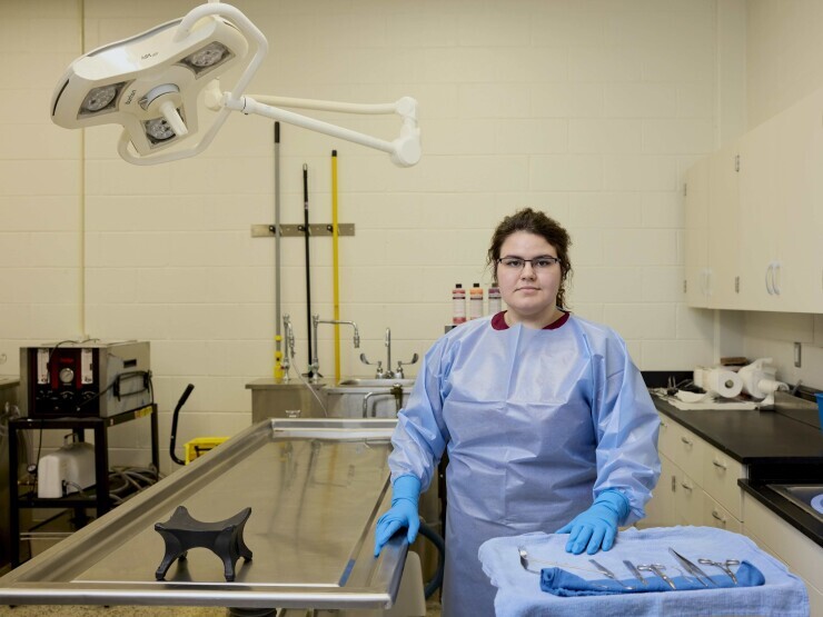 Student in the funeral services lab in Chester in protective clothing and gloves with metal tool and other embalming equipment. 