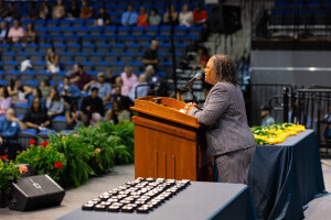 A Brightpoint professor speaks on stage at an awards ceremony, yellow roses on a table beside her. 