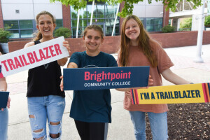 Three students laughing while standing and holding signs celebrating Brightpoint and being Trailblazers.