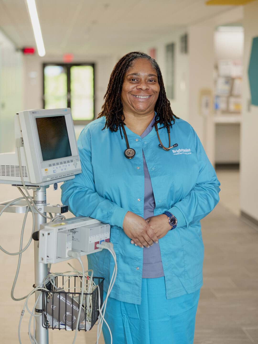 Melinda King wears blue scrubs and poses in front of nursing equipment. 
