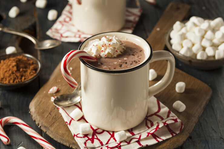 links to A mug of hot chocolate topped with whipped cream and a candy cane garnish. 
