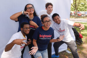 Group of students wearing Brightpoint t-shirts posing and smiling in front of a photo backdrop.