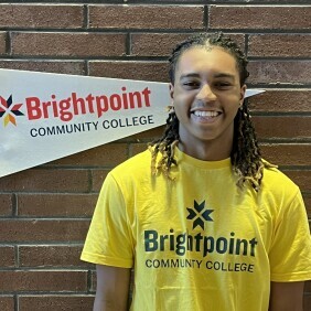 A Brightpoint student wearing a yellow Brightpoint t-shirt smiles brightly. 