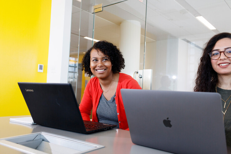 Two smiling women work on laptops in a bright, airy and modern space on Brightpoint's Midlothian Campus. 