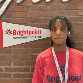 Maya, a Brightpoint Student Ambassador, smiles in front of a Brightpoint flag. 