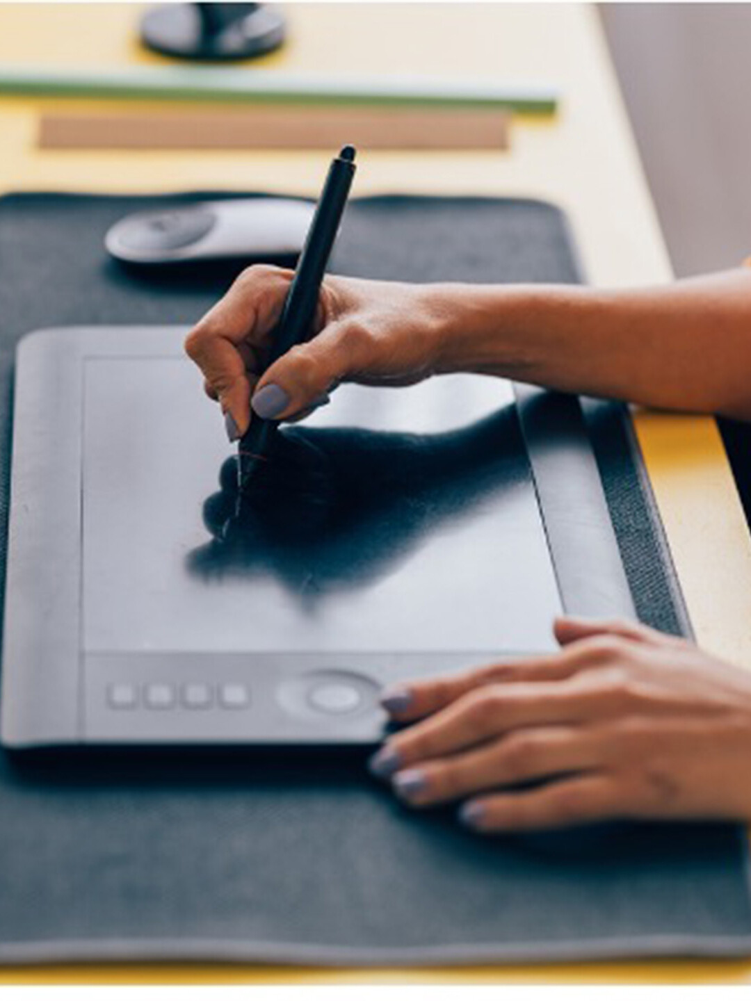 A hand uses a drawing pen to write on a drawing tablet. 