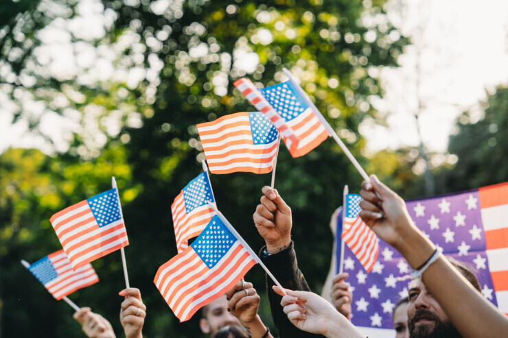 A diverse group of people wave miniature American flags outside.
