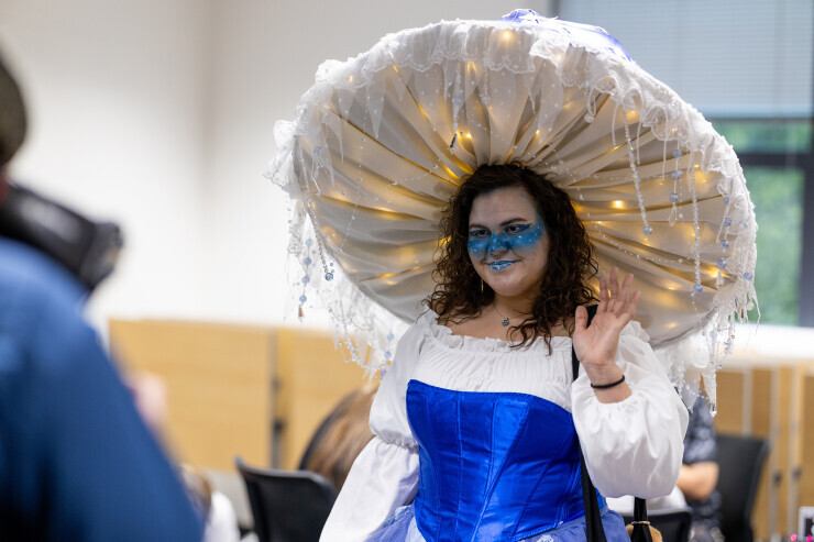 links to A person in a shimmering blue and white jellyfish costume waves to an approaching person. 