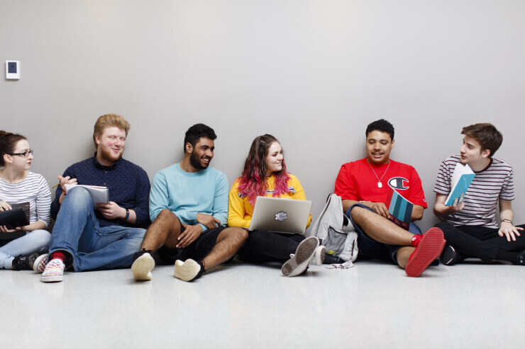 Group of students sitting on the floor, smiling, laughing and talking.