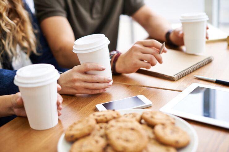 links to Hands hold coffee cups and reach for study materials on top of a desk. 