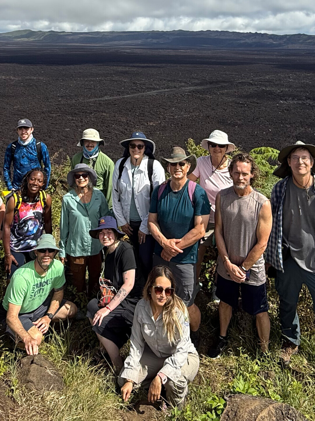 Brightpoint students enjoying a study abroad trip to the Galapagos Islands. The group poses in front of lush vegetation, with a blue sky and volcano behind them. 