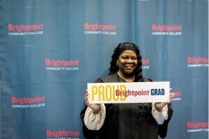 A woman in a cap and gown holds a sign in front of her that says, 