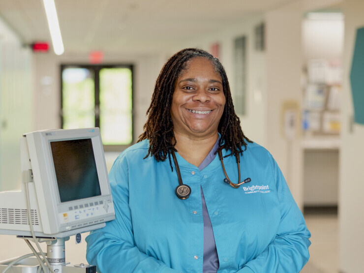 Melinda King wears blue scrubs and poses in front of nursing equipment. 