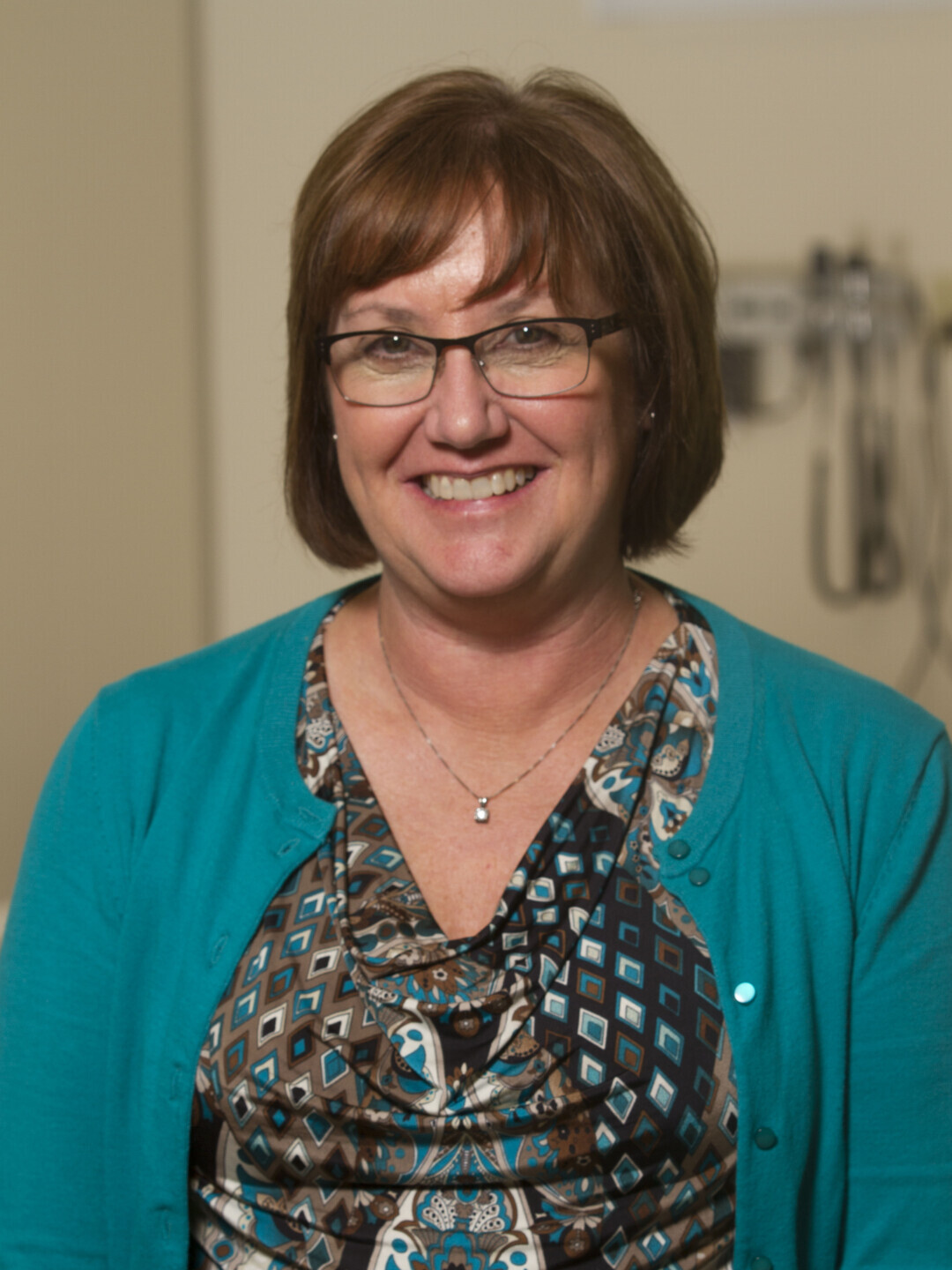 A woman wearing glasses smiles at the camera. She appears welcoming and confident. 