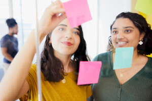 A student marks a post-it note on a glass board, preparing study notes. 