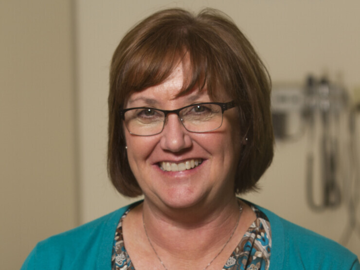 A woman wearing glasses smiles at the camera. She appears welcoming and confident.