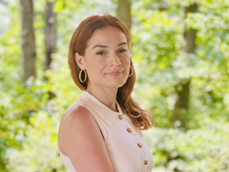 A woman in business casual clothing poses outside, her arm resting on a wooden railing.
