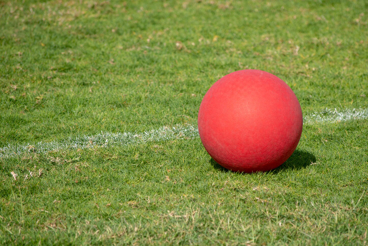 links to A bright red kickball sitting on green grass near a white line. 