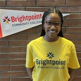 A student in a yellow Brightpoint t-shirt smiles cheerfully.