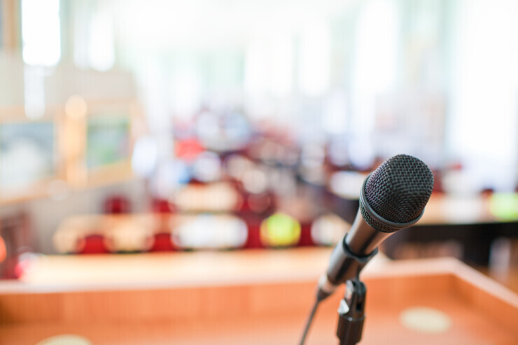 links to A microphone with a classroom in the background, representing a speech given to students. 