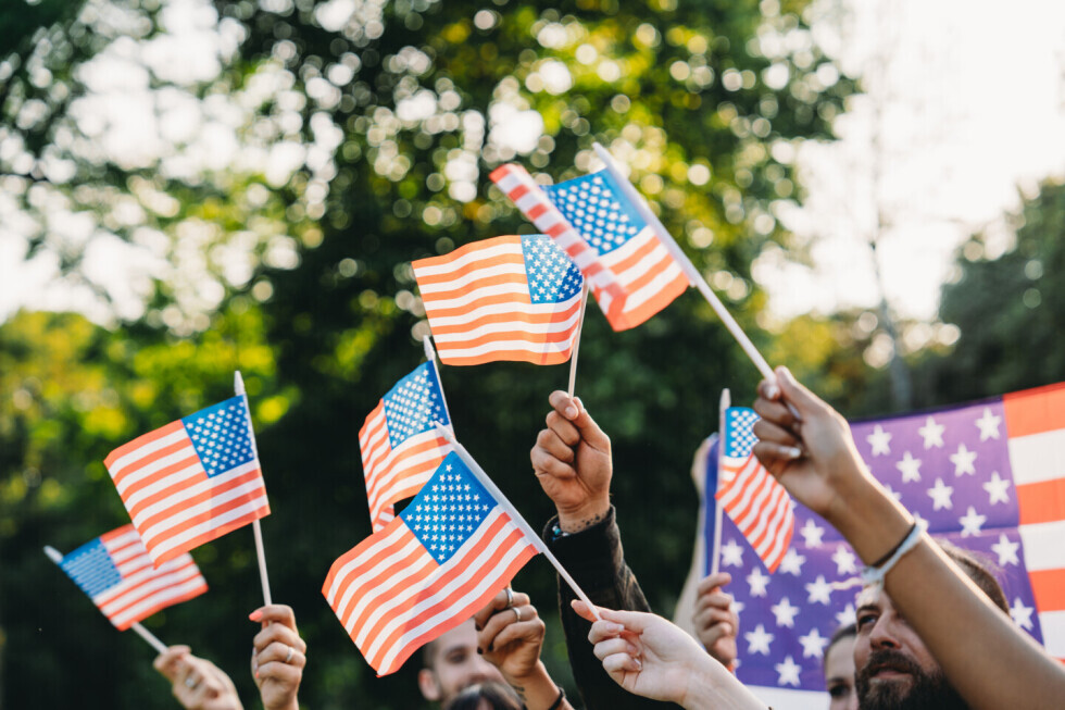 A diverse group of people wave miniature American flags outside. 