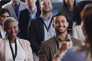 Multiple people sitting together, smiling and reacting to a speaker who has their back to the camera.