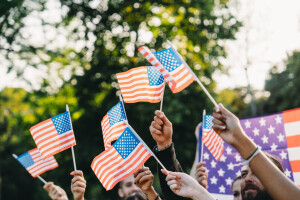A diverse group of people wave miniature American flags outside. 