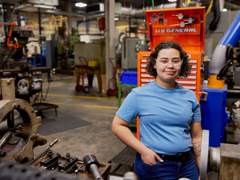Brightpoint alum Heilie Sheppard smiles while standing in front of machinery. 