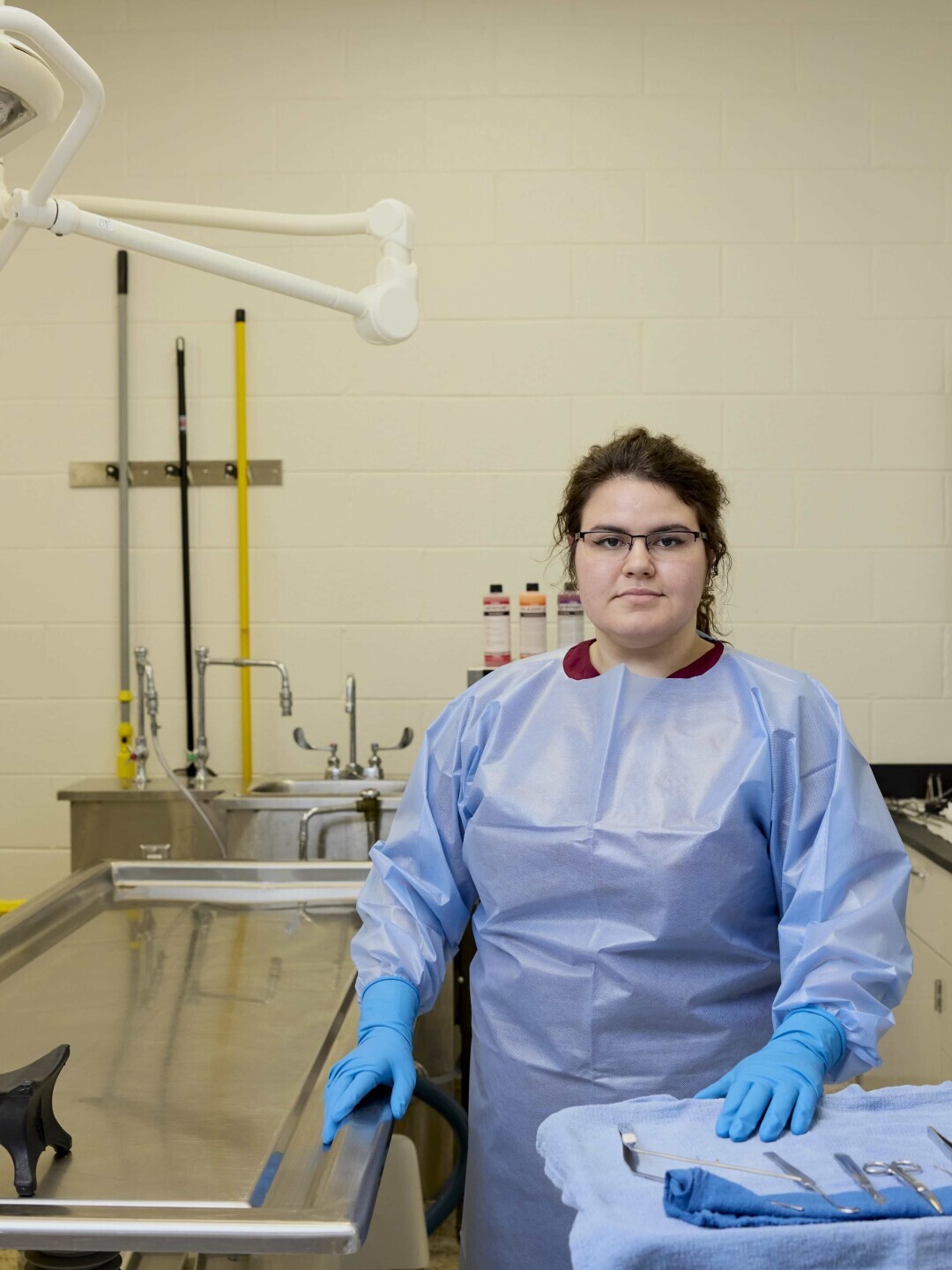 Student in the funeral services lab in Chester in protective clothing and gloves with metal tool and other embalming equipment. 
