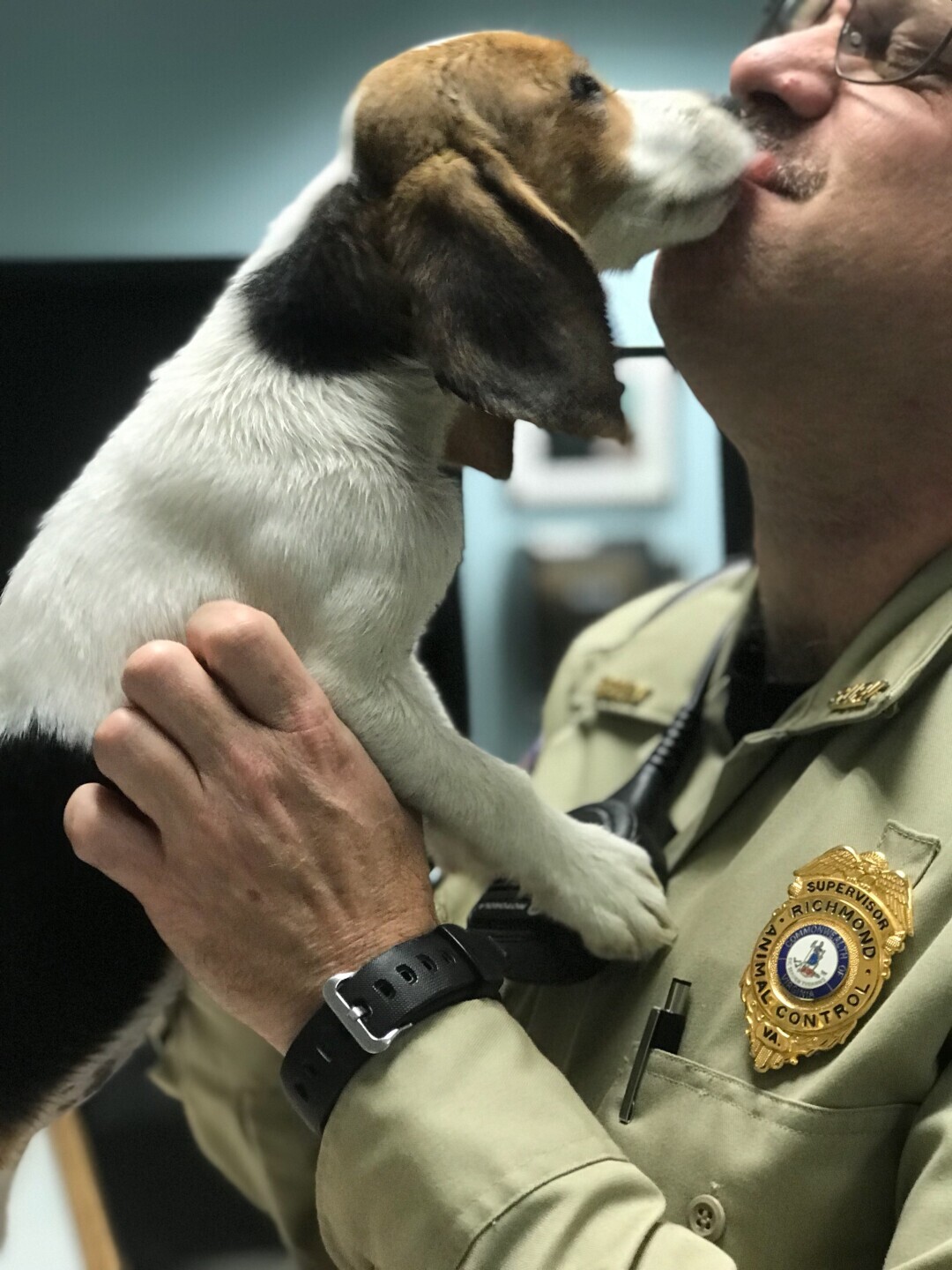 A puppy licks Rob's face as he holds it in his arms while on duty. 