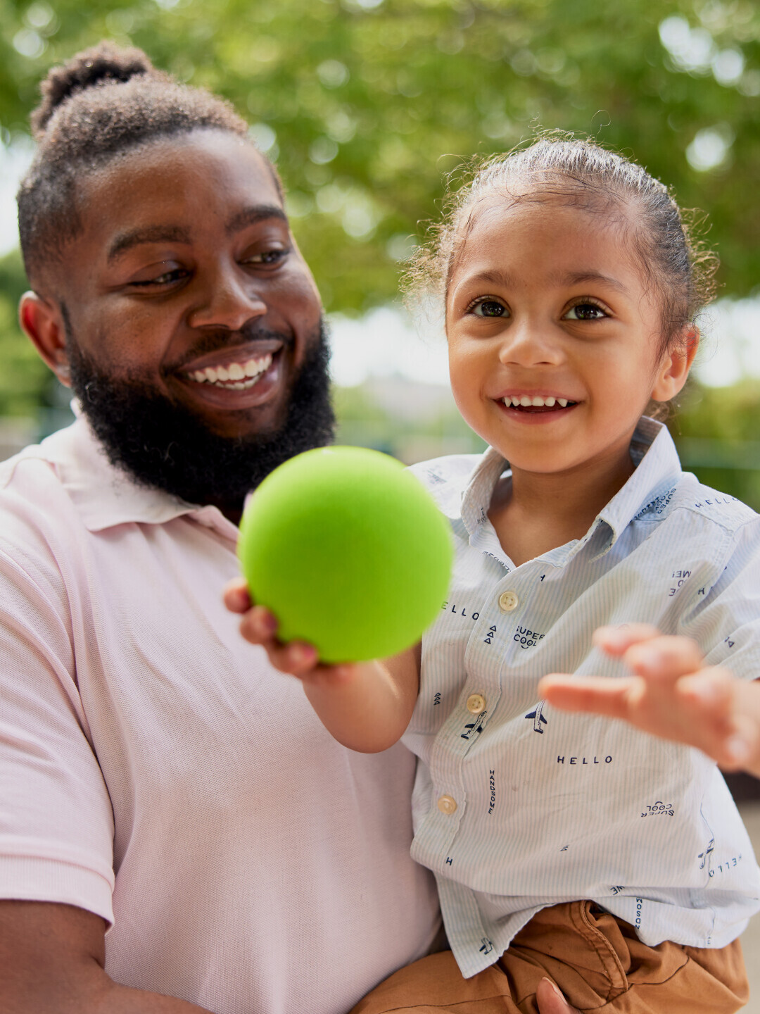 Brightpoint student Jason Taylor holds his son in his arms and smiles at him. His son is also smiling and holding a green ball. 