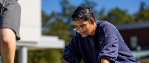 A Brightpoint student with glasses smiles and stares downwards, contemplating a decision.