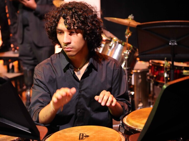A music student looks intensely at a music stand over a drum with hands poised to strike. 