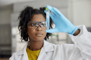 A student wearing a lab coat and safety goggles examines a test tube.