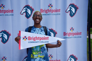 A Brightpoint alum with bright green hair smiles and holds a Brightpoint flag in her hands. 
