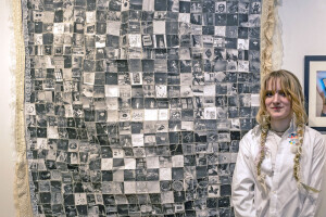 Artwork hanging on wall with artist standing in front of it