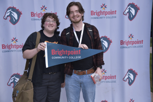 Two students pose in front of a trailblazer banner while holding a Brightpoint flag. 