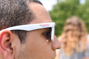 Profile of a student's face, who is looking to the right and wearing white sunglasses that have the Brightpoint logo on the frame.  